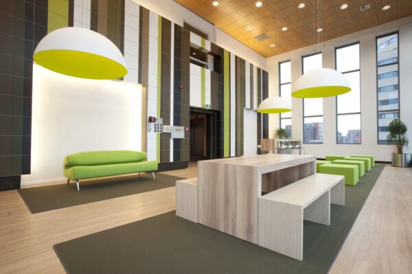 Moderne en kleurrijke lobby aan de Rivium Boulevard met groene meubels, houten zitplekken en grote hanglampen.